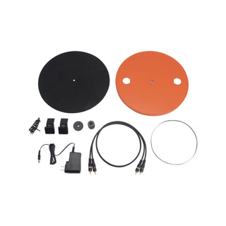 A multi-piece electronic audio or lighting control kit laid out on a white background, including two circular signal or control plates (one black, one orange), a power adapter, cables, connectors, and small mounting hardware.