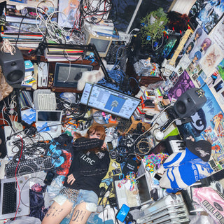 Person sitting amidst a chaotic pile of electronic equipment and personal items
