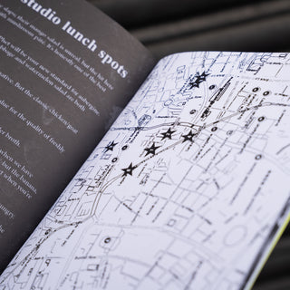 An open notebook or journal lying on a dark ribbed surface, showing a dark left page with text and a white right page with a black map-style illustration and star markers.