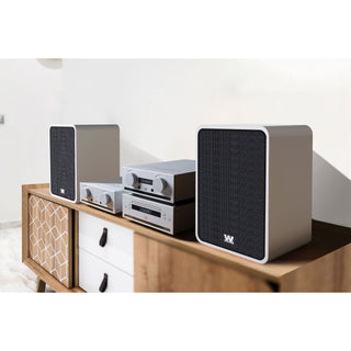 A modern  audio speaker system with two tall side speakers and a central multi-level receiver stack, styled on a wooden cabinet against a white wall.